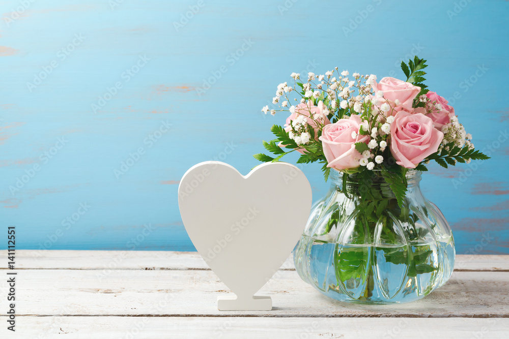 Wall mural rose flower bouquet in glass vase and heart shape sign over wooden background