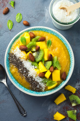 Mango smoothie bowl with pieces of kiwi, mango, coconut shavings and chia seeds on a stone background. Selective focus.