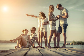 Friends sitting on wooden pier under sunset light.