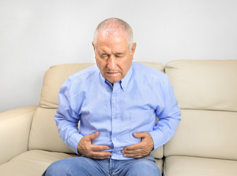 Senior man suffering stomach ache sitting on a couch in the living room at home