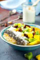 Mango smoothie bowl with pieces of kiwi, mango, coconut shavings and chia seeds on a stone background. Selective focus.