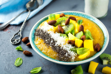 Mango smoothie bowl with pieces of kiwi, mango, coconut shavings and chia seeds on a stone background. Selective focus.