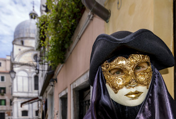 A characteristic and beautiful Venetian mask worn by a woman with gorgeous blue eyes in the historic center of Venice, Italy