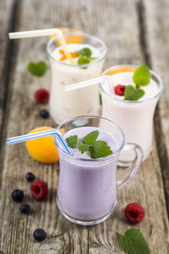 Three glasses with smoothies  or yogurt with fresh berries on a wooden table.