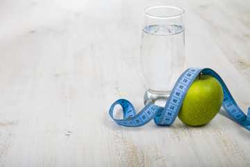 Green apple,glass of water and measuring tape on a wooden table.