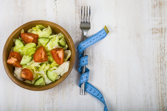 Salad in wooden bowl, fork and measuring tape on a table close-up.
