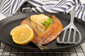  smoked kipper with lemon, butter and parsley on a pan