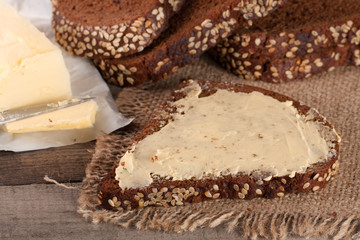 slices of black bread with sesame seeds and butter on an old wooden background