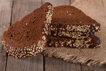 slices of black bread with sesame seedson on the old wooden background