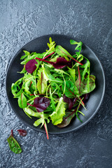 Mix fresh leaves of arugula, lettuce, spinach, beets for salad on a dark stone background. Selective focus.