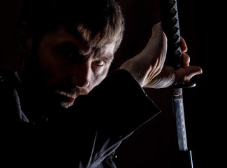 stern angry businessman in a wool coat with sword in dark background