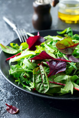 Mix fresh leaves of arugula, lettuce, spinach, beets for salad on a dark stone background. Selective focus.