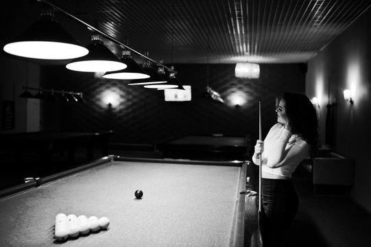 Young curly girl posed near billiard table. Sexy model at black mini mini skirt play russian snooker. Play game and fun concept.