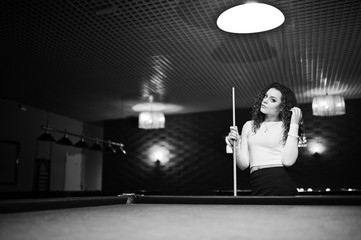 Fototapeta na wymiar Young curly girl posed near billiard table. Sexy model at black mini mini skirt play russian snooker. Play game and fun concept.