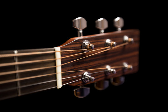 The upper part of the guitar on a black background with the strings, nut and tuning pegs, dark wood, blur