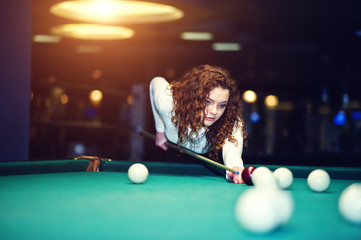 Young curly girl posed near billiard table. Sexy model at black mini mini skirt play russian snooker. Play game and fun concept. - obrazy, fototapety, plakaty