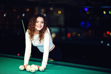 Young curly girl posed near billiard table. Sexy model at black mini mini skirt play russian...