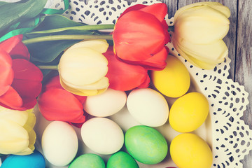 Colored easter eggs with tulips on a white wooden background.