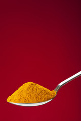 spoon of ground turmeric on red background