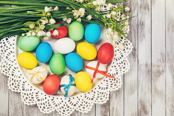 Easter background. Colored easter eggs and spring flowers on white wooden background.