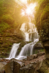 Fototapeta na wymiar Amazing beauty of Alps mountains waterfall. Summer waterfall in Alps with soft sun rays at evening