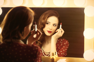 photo of beautiful young woman holding her lipstick near the window with lights