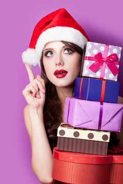 photo of beautiful young woman with gifts in santa claus hat on the wonderful purple background