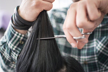 Close up of a male hairdresser cutting clients hair with scissors at beauty salon.