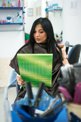 Attractive brunette girl is choosing hair color from the catalog in hair salon.