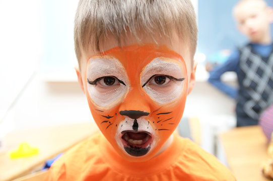 Make up artist making tiger mask for child.Children face painting. Boy  painted as tiger or ferocious lion. Preparing for theatrical performance. Boy actor playing role. Tiger mask face