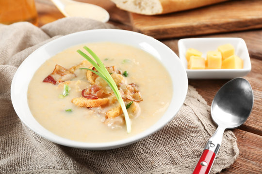 Delicious beer cheese soup with onion and fried bacon on table