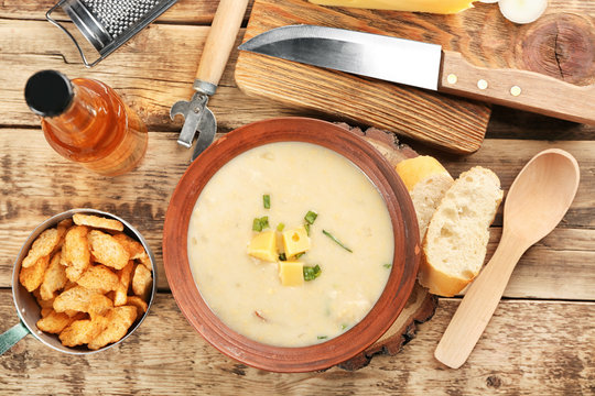 Delicious beer cheese soup with croutons and onion on table