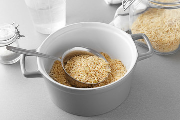 Saucepan with raw brown rice on table