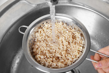 Washing raw brown rice in colander over kitchen sink