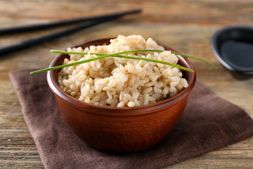 Bowl with brown rice on wooden table background