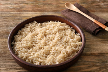 Plate with brown rice on wooden table background