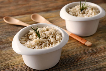 Two bowls with brown rice on wooden table background