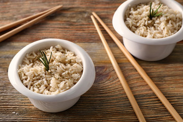 Two bowls with brown rice on wooden table background