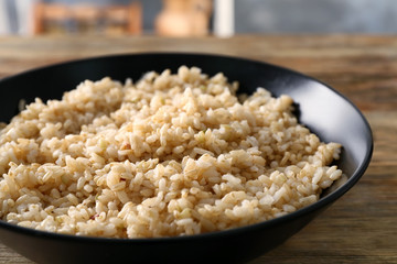 Plate with brown rice on wooden table