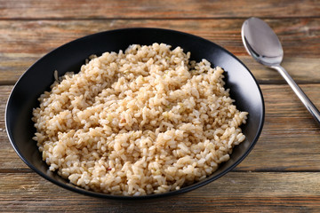 Plate with brown rice on wooden table background