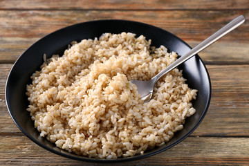 Plate with brown rice on wooden table background