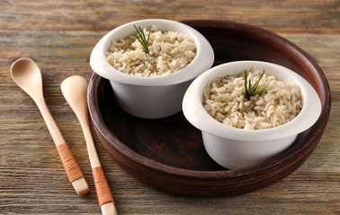 Two bowls with brown rice on wooden table background