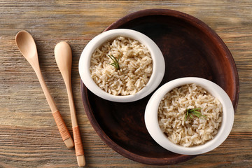 Two bowls with brown rice on wooden table