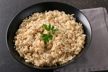 Plate with brown rice on gray table background