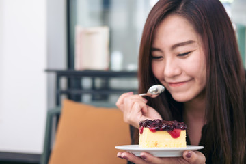 A woman holding and eating blueberry cheese cake in ceramic plate with spoon in modern cafe