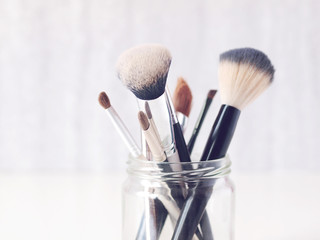 Set of makeup brushes in a glass jar on light background