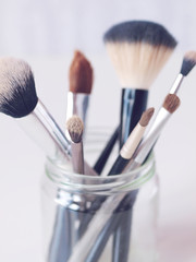 Set of makeup brushes in a glass jar on light background