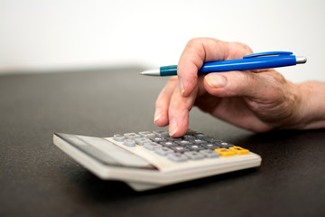Close-up photo of senior woman's hand using calculator and pen to calculate tax.