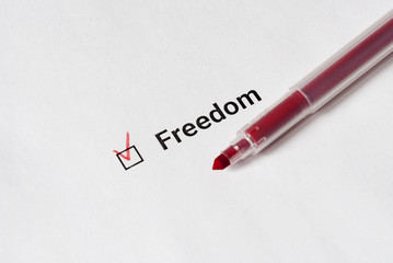 Checklist. Red pen and the inscription Freedom with check mark on the white paper