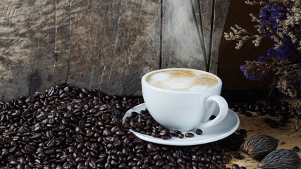 Hot cappuccino with streamed milk. Pour the hot latte art by milk. A cup of strong espresso coffee put on the wood table with shiny dark roasted Italian coffee beans. Aroma and flavor coffee beverage.